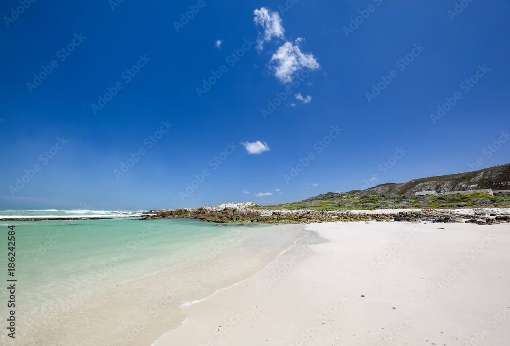 Beach view with white sand, rocks and crystal clear water at Brandfontein - Rietfontein Nature Reserve near Cape Agulhas, Western Cape Province, South Africa.