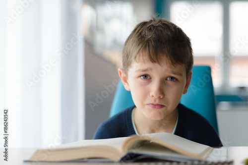 Tired 8 years old boy doing his homework at the table