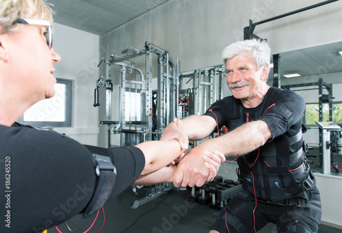 Pärchen im mittleren alter trainiert im Fitnessstudio mit einem EMS Gerät Stromimpulsgerät, Gummibänder, Kurzhanteln photo