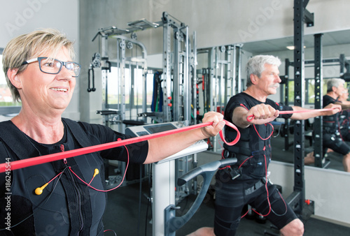 Pärchen im mittleren alter trainiert im Fitnessstudio mit einem EMS Gerät Stromimpulsgerät, Gummibänder, Kurzhanteln photo