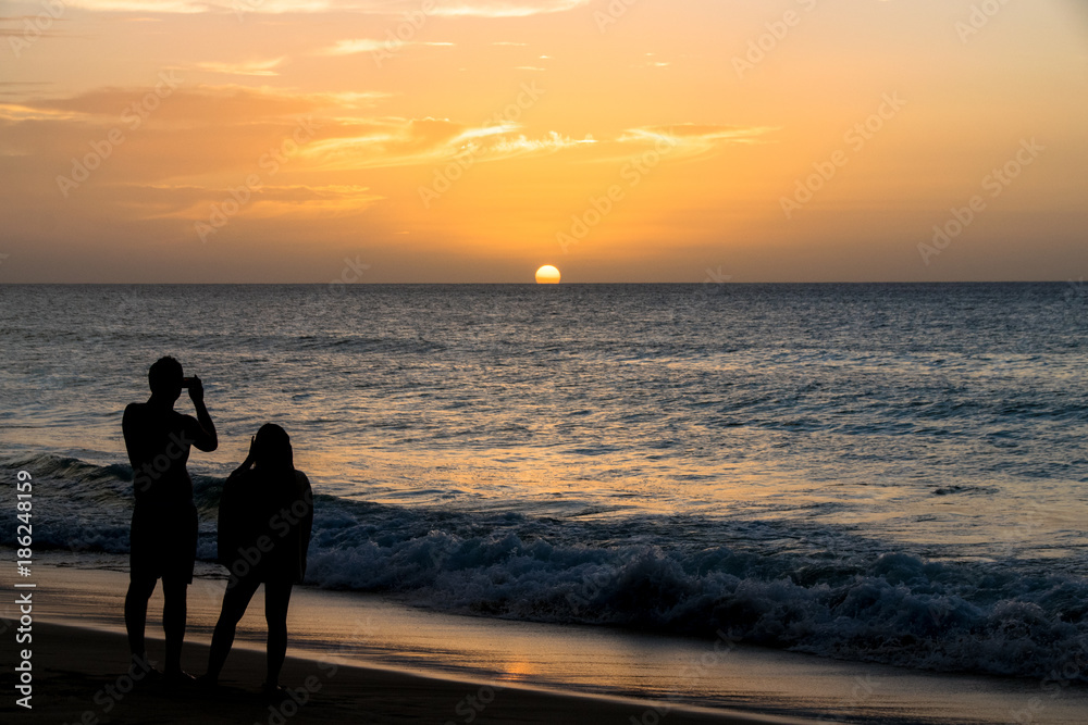 Fototapeta premium Silhouette of a couple taking photos of the sunset over the ocean