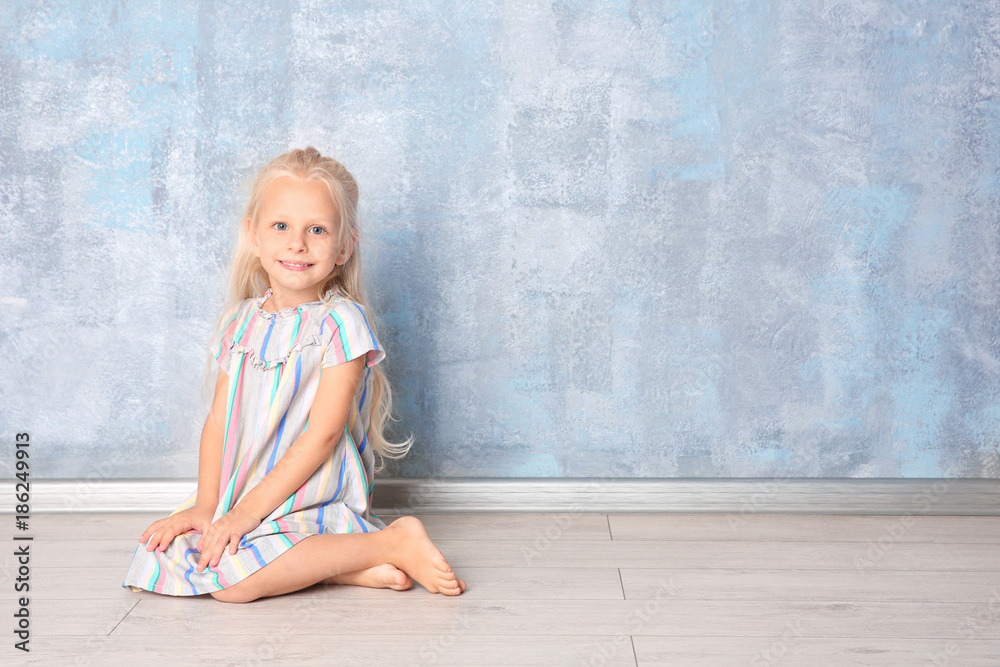 Fototapeta premium Cute little girl sitting near grey wall