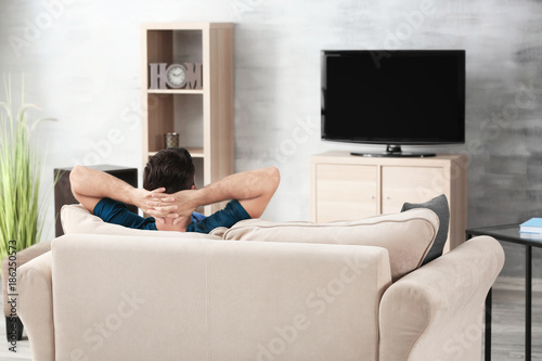 Handsome man watching TV while resting on sofa at home © Africa Studio