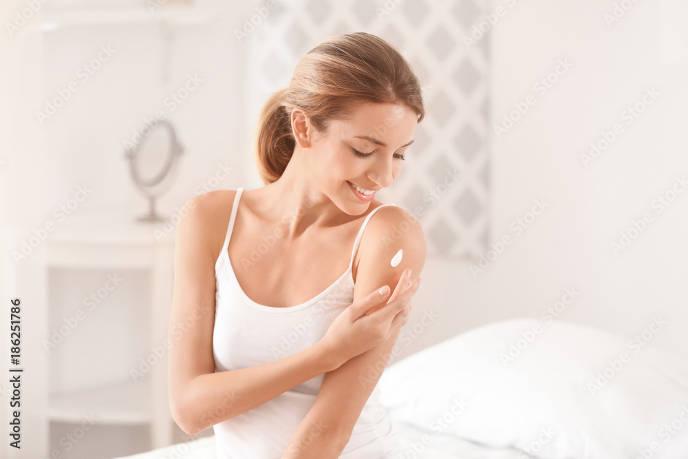 Young woman applying body cream at home - obrazy, fototapety, plakaty 
