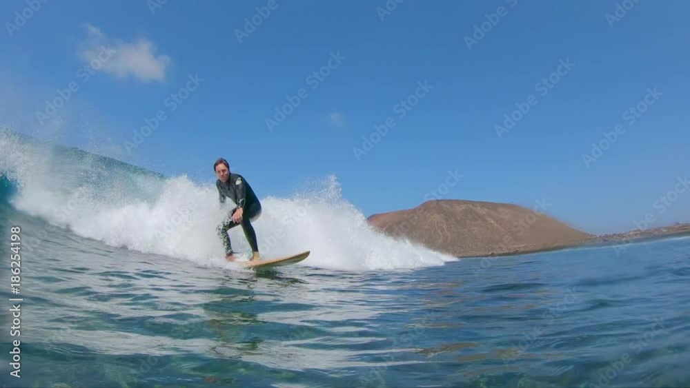 SLOW MOTION, LOW ANGLE, UNDERWATER Cheerful young surfboarder rides awesome waves in Lobos. Surfer riding awesome big wave near volcanic island. Fun ocean waves splashing as surfer rides past camera.