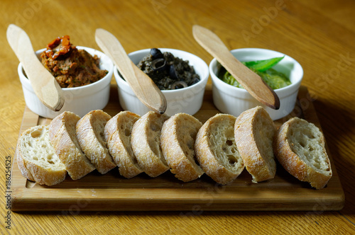 Spreads and bread rolls served on a wooden board.