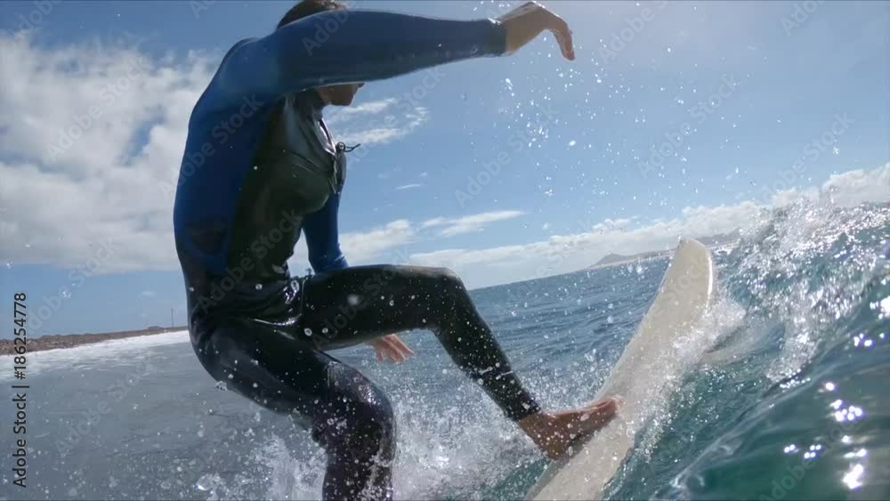 SLOW MOTION CLOSE UP: Male surfer riding blue breaking waves on a sunny day. Focused surfer carving wave and making sharp turn on his surfboard in awesome Fuerteventura. Young man having fun surfing.