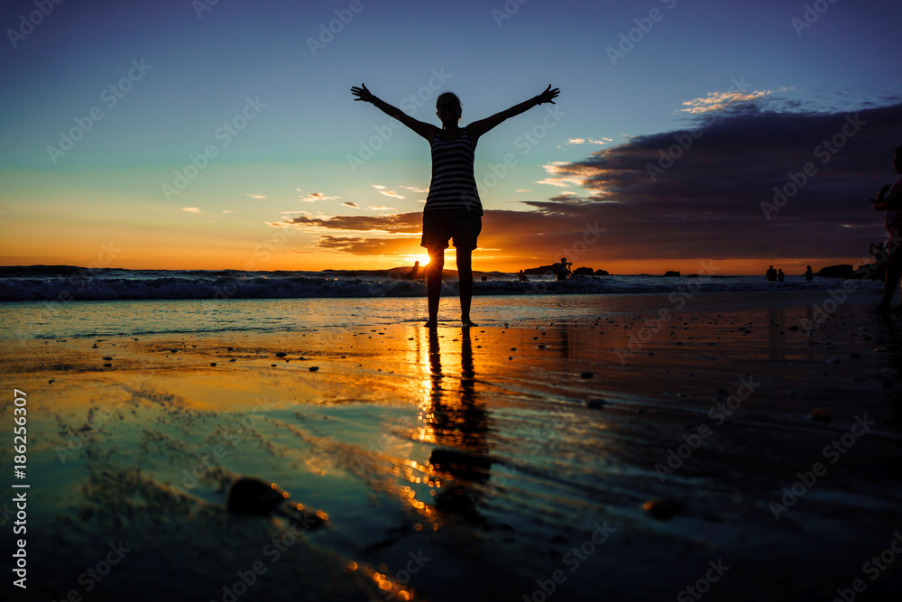 Freedom concept. silhouette girl with open arms walking on sand beach during sunset. Reflections