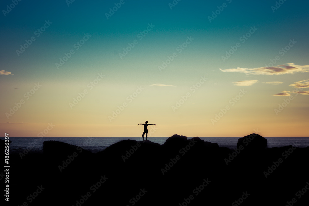 Silhouette of woman on sunset beach, girl with open arms over sea coast. Freedom concept