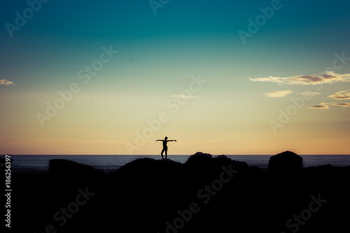 Silhouette of woman on sunset beach, girl with open arms over sea coast. Freedom concept