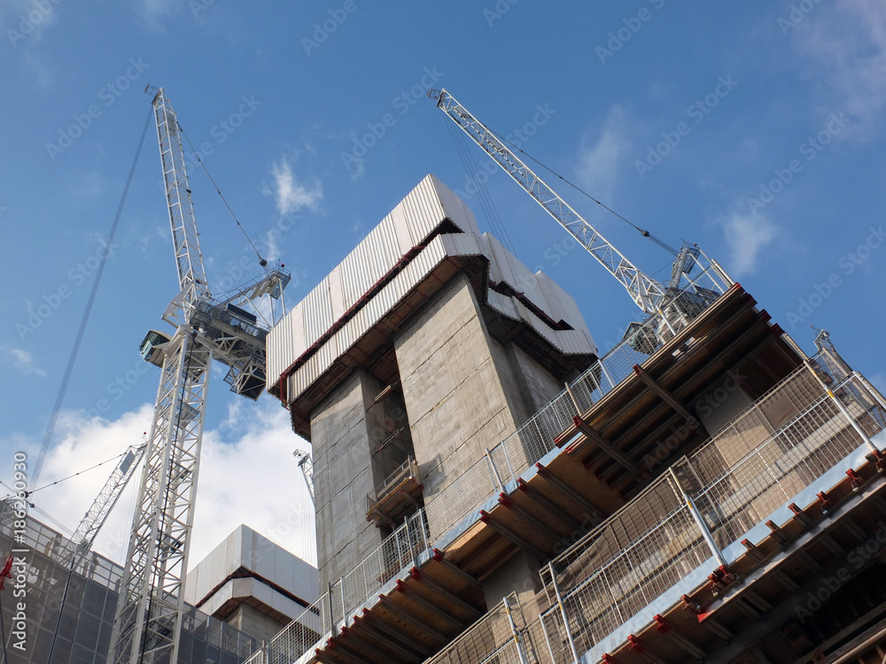 cranes working on a large modern construction site with concrete structures and blue sky