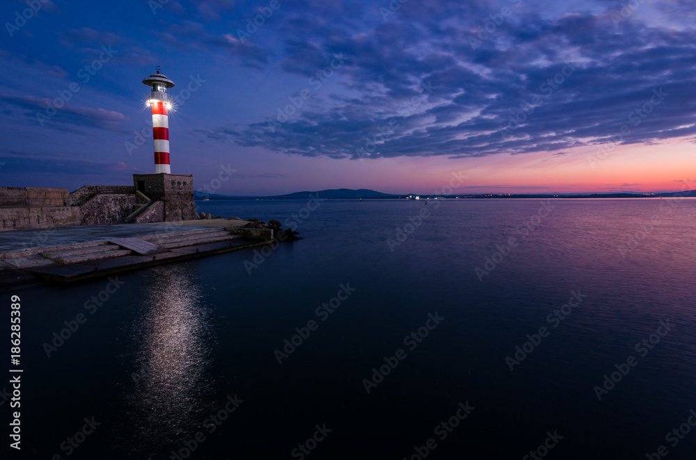 colored sunset and lighting lighthouse on the sea coast