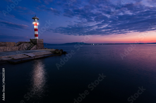 colored sunset and lighting lighthouse on the sea coast photo
