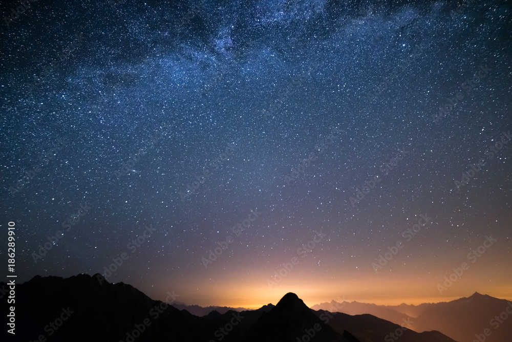 Fototapeta premium The wonderful starry sky on Christmas time and the majestic high mountain range of the Italian Alps, with glowing villages below.