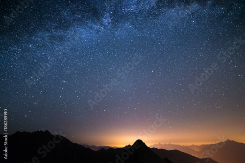 The wonderful starry sky on Christmas time and the majestic high mountain range of the Italian Alps, with glowing villages below.
