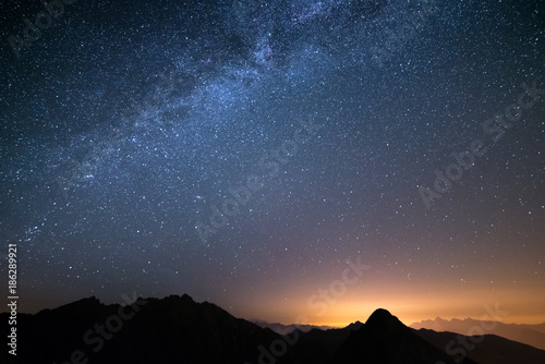 The wonderful starry sky on Christmas time and the majestic high mountain range of the Italian Alps, with glowing villages below.