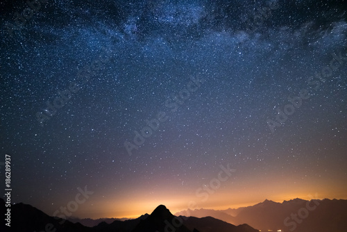 The wonderful starry sky on Christmas time and the majestic high mountain range of the Italian Alps, with glowing villages below.