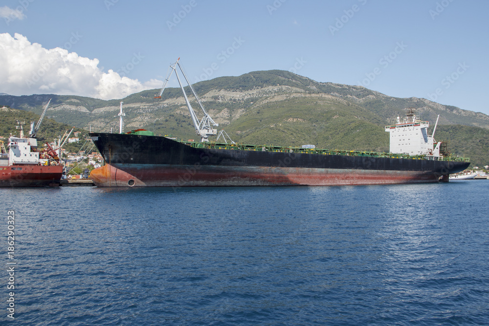 Moored tanker near the shore against the backdrop of green mountains in the summer.