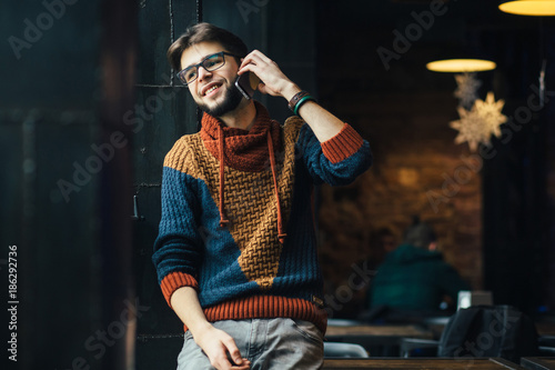 Handsome successful ceo man talking with smart phone near the big window at his work station in a modern office, in dark interior, lights. He looks happy and relaxing. photo