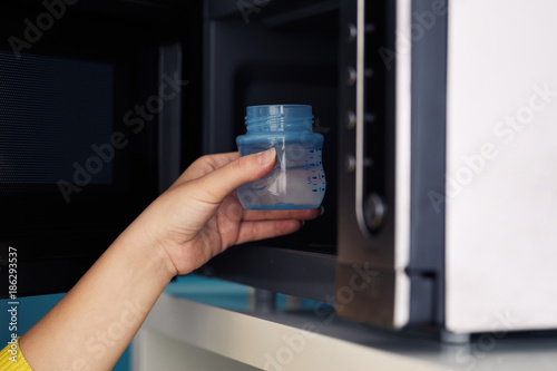 Close up of female hand putting a baby bottle with water into a microwave