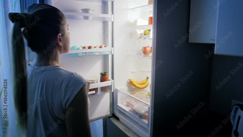 Slow motion video of young woman looking for food in refrigerator at night Slow motion video of young woman looking for food in refrigerator at night