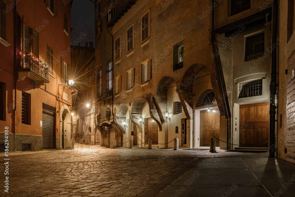 ancient old street of bologna in italy at night with lantern lights and stone paving