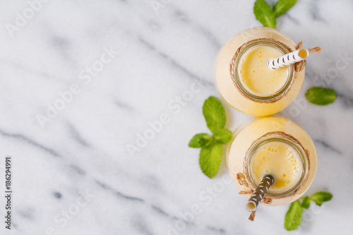 Top view of yellow fruit smoothies in the glass bottles with straw on the white marble