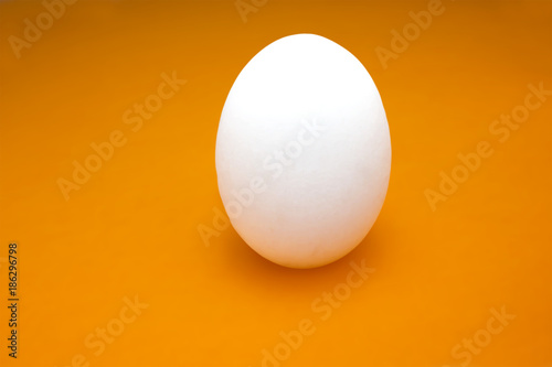 A photo of uncooked hen white egg on the orange table, colorful rustic background.
