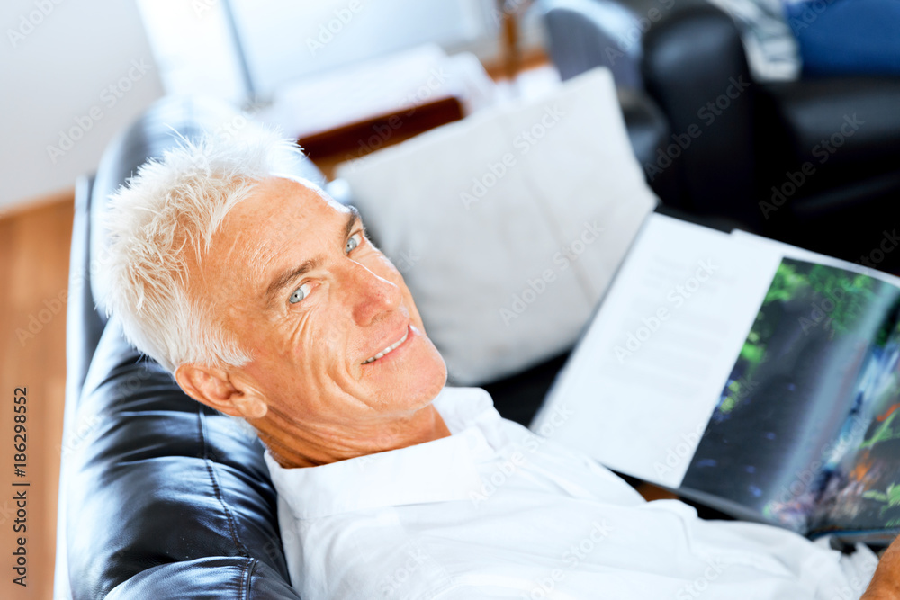 Fototapeta premium Handsome sennior man reading a book relaxing on a sofa