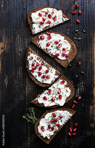 Fototapeta Naklejka Na Ścianę i Meble -  Open sandwiches rye bread with cream cheese and pomegranate seeds, flakes of almond  on marble surface. Healthy snack concept. Top view.