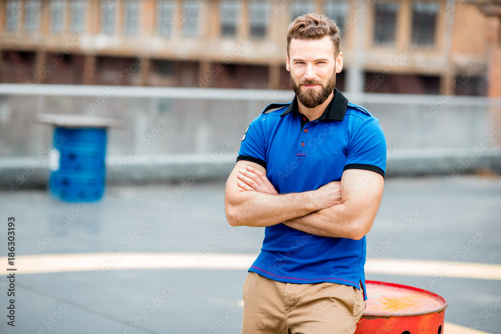 Lifestyle portrait of a handsome man in blue t-shirt sitting on a barrel outdoors on the helicopter platform Lifestyle portrait of a handsome man in blue t-shirt sitting on a barrel outdoors on the helicopter platform