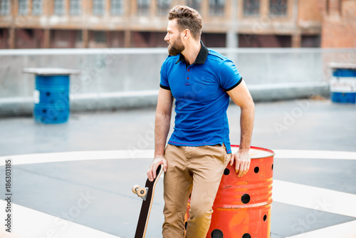 Lifestyle portrait of a handsome man in blue t-shirt sitting with skateboard outdoors on the helicopter platform