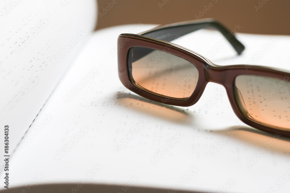 Braille book for low vision/ blind person reading the sign, eyeglasses background Braille book for low vision/ blind person reading the sign, eyeglasses background