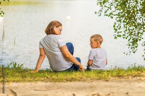 Mother and son playing on the grass in the Park looking at the lake.
