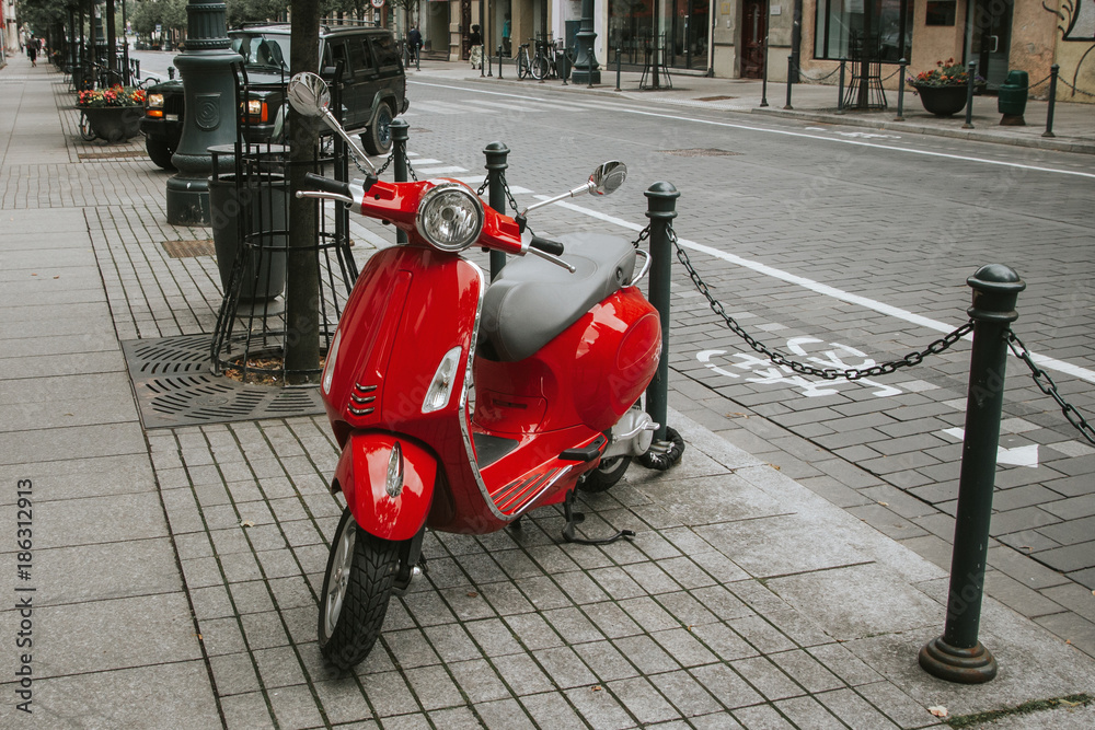 Fototapeta premium Red scooter parked on the pavement. Europe street photo background.