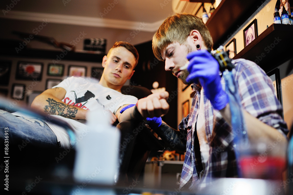 Obraz premium tattoo artist makes a new tattoo to a young guy on his arm in a tattoo parlor