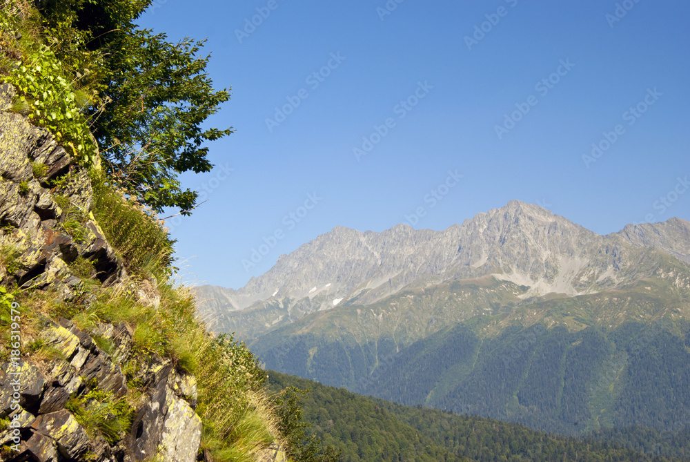 Caucasian autumn mountain landscape in clear weather with a grassy rock in the foreground and a distant ridge in the background Caucasian autumn mountain landscape in clear weather with a grassy rock in the foreground and a distant ridge in the background