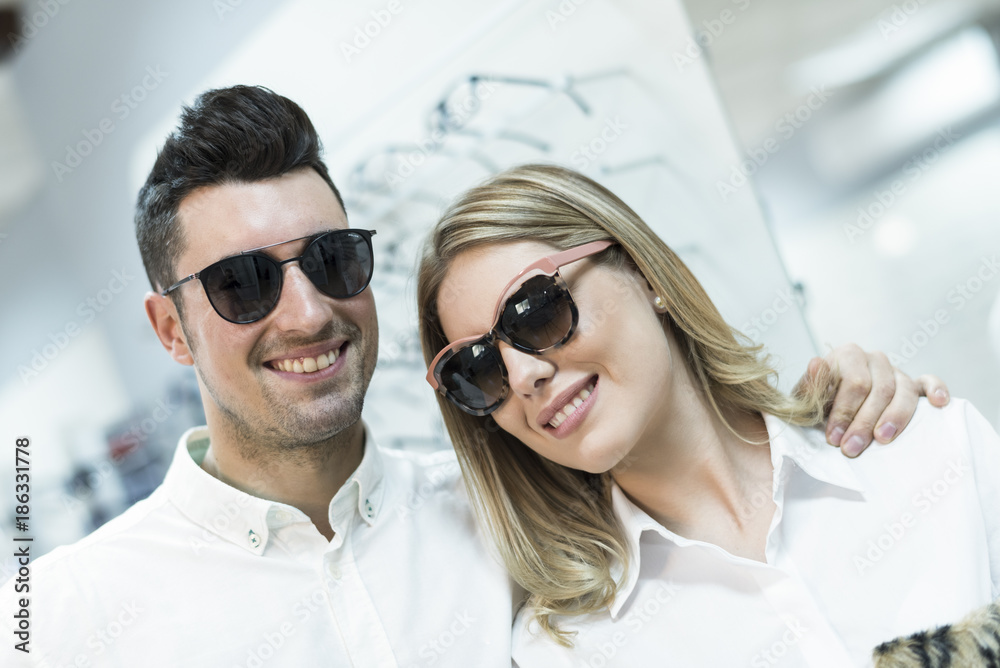 Couple with sunglasses smiling and looking at camera in glasses store optometry shop