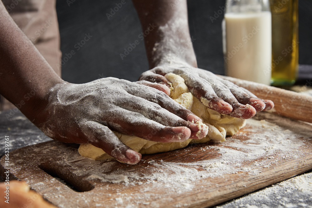 Mans hands kneading dough on wooden board