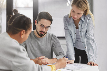 Creative team of three mixed race members have workshop, sit in coworking space, try to solve problem with documentation, collaborate for common project. Business successful people check accountings