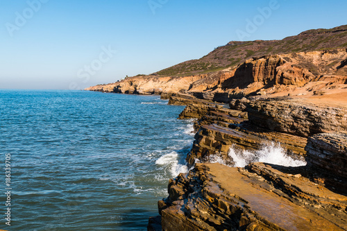 A wave crashes on the sea and wind eroded cliffs in the Point Loma tidepool area of Cabrillo National Monument in San Diego, California.