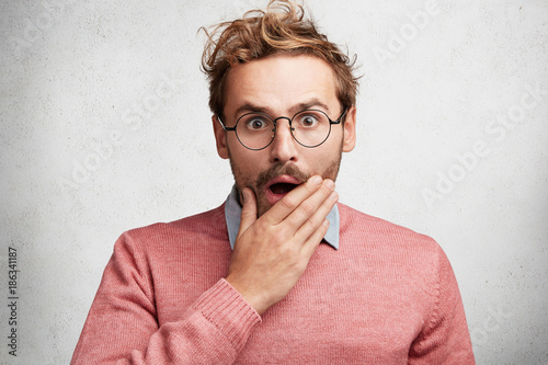 Scared shocked man looks in puzzlement and bewilderment, doesn`t believe at horrorful news, expresses great surprisment, dressed elegantly. Male geek in spectacles horrified to fail final exam photo