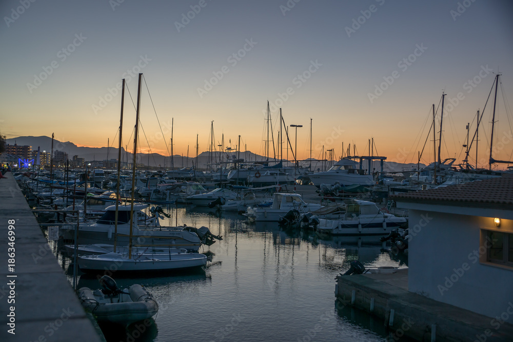 Fototapeta premium Sunset view of a marina with sailing and motor boats and a mountainous landscape in the background