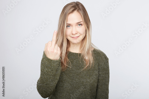 Middle finger sign. Cute blond Caucasian lady shows bad gesture to man who hurts her, needs revenge. European attractive lady with flirty smile can defend herself. People, emotions and expression. © Yulia
