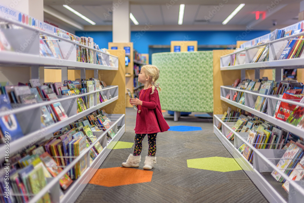 Young preschool girl choosing books from the many choices at the library