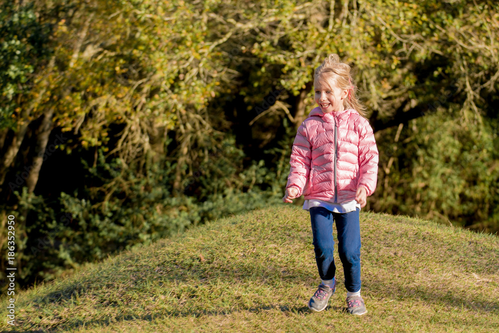 Happy little girl smiling, with ponytail, running on grassy hill in the park Happy little girl smiling, with ponytail, running on grassy hill in the park