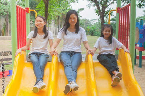 Adorable and Holiday Concept : Woman and cute little children feeling funny and happiness on a slide at playground in the park. © Angkana