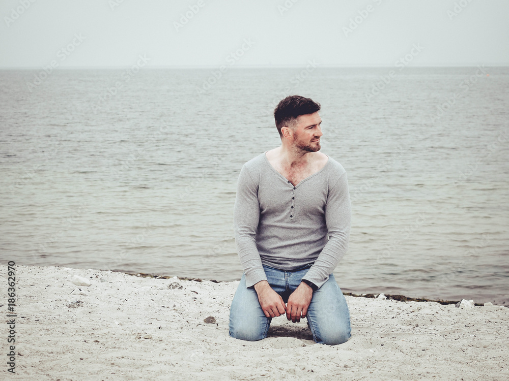 handsome guy sitting on the sand on the beach and looking out into the distance on the sea handsome guy sitting on the sand on the beach and looking out into the distance on the sea