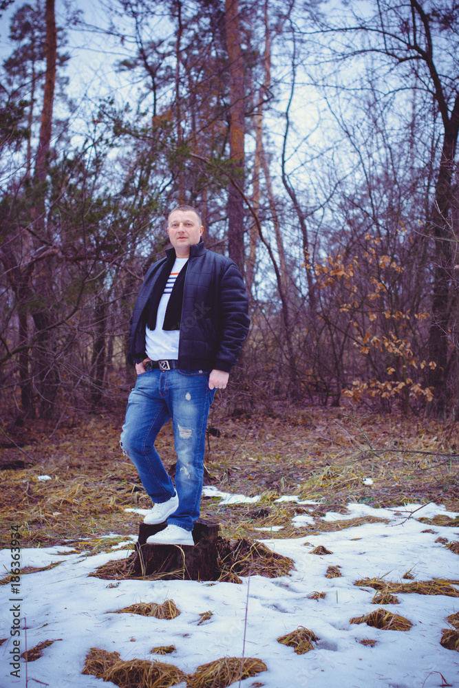 Fototapeta premium Portrait of a middle age man in warm clothing at forest on a cold day. Fashion handsome elegant man wearing black coat in winter day over trees forest background 