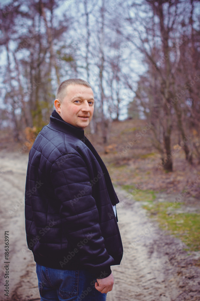 Portrait of a middle age man in warm clothing at forest on a cold day. Fashion handsome elegant man wearing black coat in winter day over trees forest background Portrait of a middle age man in warm clothing at forest on a cold day. Fashion handsome elegant man wearing black coat in winter day over trees forest background